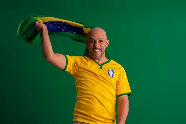 Afro brazilian man supporter of the brazilian football team in\
the 2022 cup with the flag of brazil and with a facial face