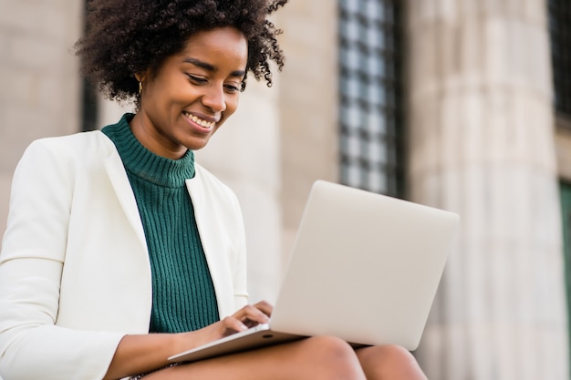 Donna d'affari afro utilizzando il suo computer portatile mentre era seduto sulle scale all'aperto. concetto urbano e aziendale.