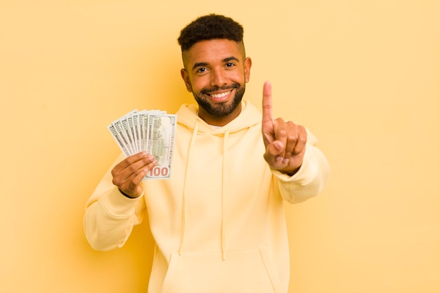 Afro cool man smiling proudly and confidently making number one dollar banknote concept