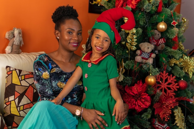 Afro-descendant Colombian Latins mother and daughter sitting on the sofa next to the Christmas tree