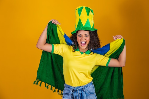 Afro girl cheering for favorite brazilian team, holding\
national flag in yellow background.