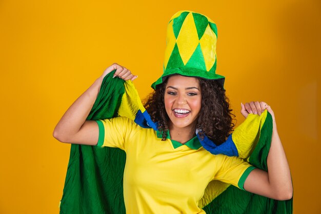 Afro girl cheering for favorite brazilian team, holding national flag in yellow background