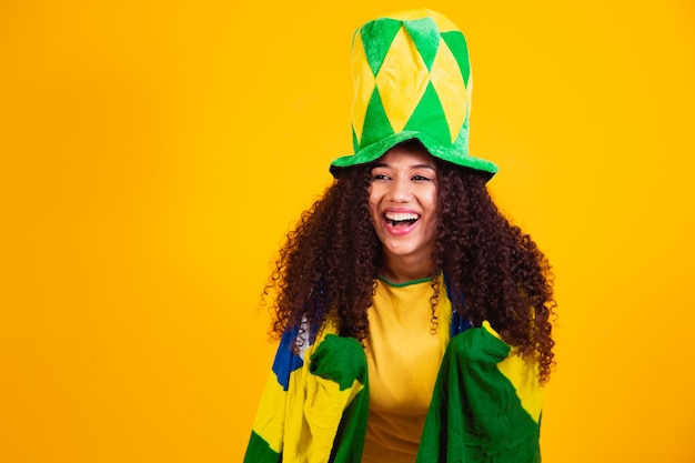 Afro girl cheering for favorite brazilian team, holding national flag in yellow background.