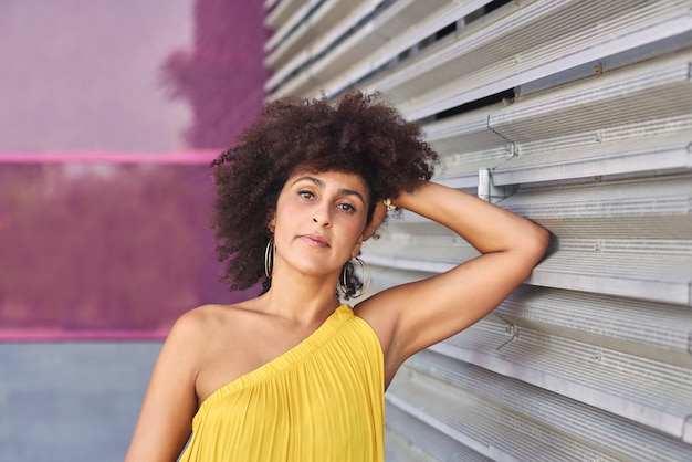 Foto donna mulatta dai capelli afro in un vestito giallo e sfondo viola.