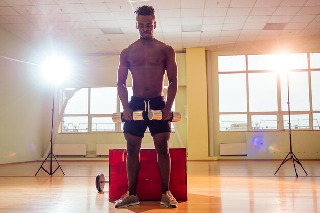 Afro holding dumbbells workout for abc press and hands in gym windows background