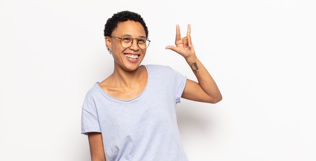 Afro jonge zwarte vrouw die zich gelukkig, leuk, zelfverzekerd, positief en rebels voelt, rock of heavy metal bord met de hand maakt