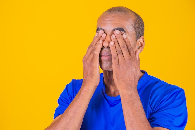 Afro-man die ogen bedekt met handen op gele achtergrond