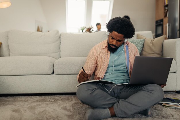 Afro-man die thuis werkt in de knusse woonkamer terwijl hij technologie gebruikt