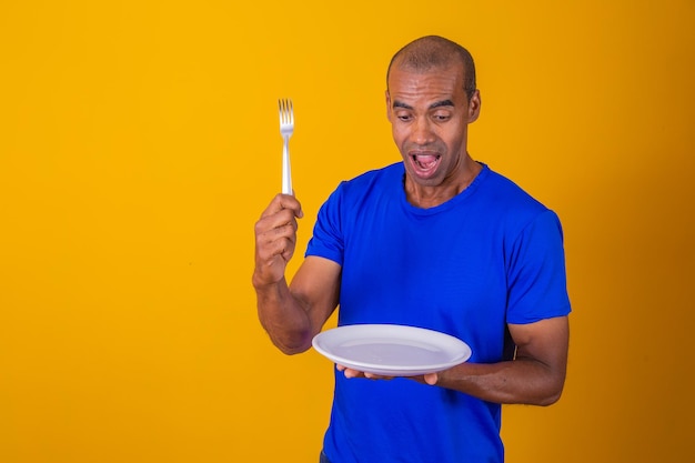 Afro man holding empty plate and fork with isolated on yellow background Copy space and mock up