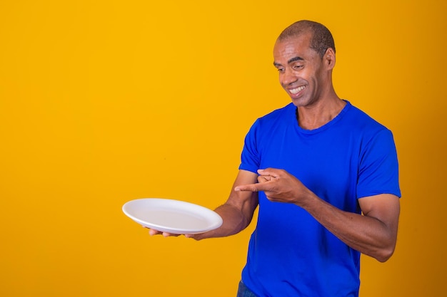 Afro man holding empty plate on yellow background