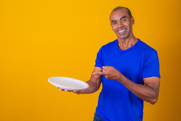 Afro man holding empty plate on yellow background