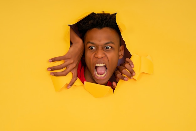 Uomo afro che guarda attraverso un buco strappato nel muro di carta.