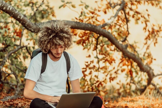 An afro man sitting in nature and using a laptop for an online meeting during a coronavirus pandemic. High quality photo