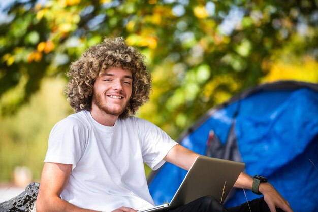 An afro man sitting in nature and using a laptop for an online meeting during a coronavirus pandemic