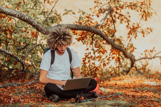 An afro man sitting in nature and using a laptop for an online meeting during a coronavirus pandemic