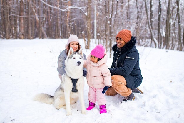 Afro man with his caucasian wife having fun with a beautiful daughter playing husky in snowy park