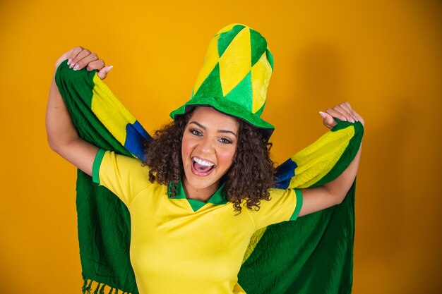 Foto afro meisje juichen voor favoriete braziliaanse team, met nationale vlag op gele achtergrond.
