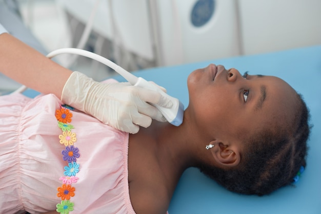 Afro meisje liggend op bed terwijl echografie van de schildklier.