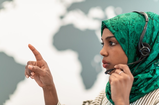 Foto donna d'affari afro musulmana con sciarpa hijab verde rappresentante del cliente donna d'affari con auricolare telefonico che aiuta e supporta online con il cliente in un moderno call center. foto di alta qualità