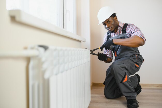 afro repairman in overalls using tools while installing or repairing heating radiator