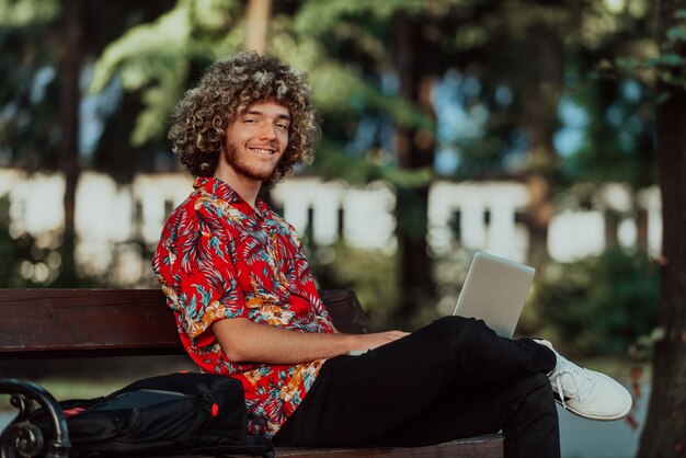 An afro teenager uses a laptop for an online meeting while sitting on a park bench