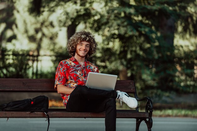 Un adolescente afro usa un laptop per una riunione online mentre è seduto su una panchina del parco