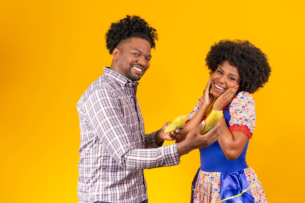 Afro valentine couple in festa junina clothes holding a tamale on yellow background