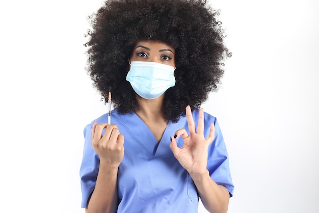 Afro-vrouw arts met medisch masker en spuit met vaccin, maakt ok gebaar