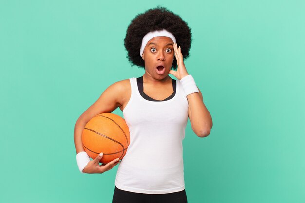 Afro-vrouw die blij, verbaasd en verrast kijkt, glimlacht en verbazingwekkend en ongelooflijk goed nieuws realiseert. basketbal concept