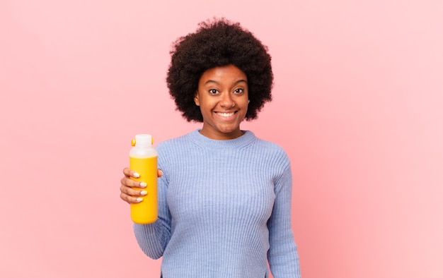 Afro-vrouw die er blij en aangenaam verrast uitziet, opgewonden met een gefascineerde en geschokte uitdrukking. smoothy concept