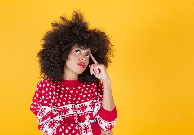 Afro-vrouw die kerstkleding draagt, denkt, gele achtergrond