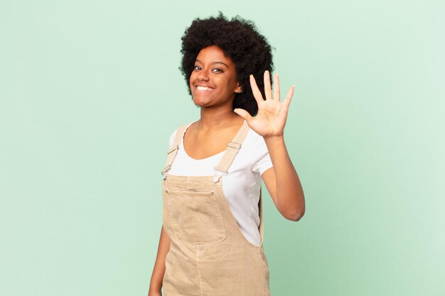 Afro-vrouw die lacht en er vriendelijk uitziet, nummer vijf of vijfde toont met de hand naar voren, aftellend chef-kokconcept