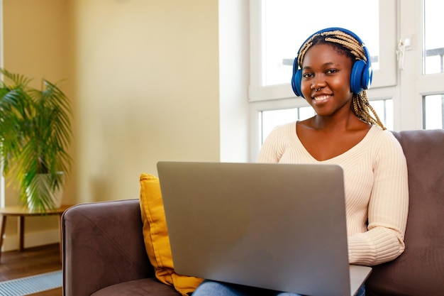 Afro-vrouw die met een laptop werkt en audioles luistert in de woonkamer thuis