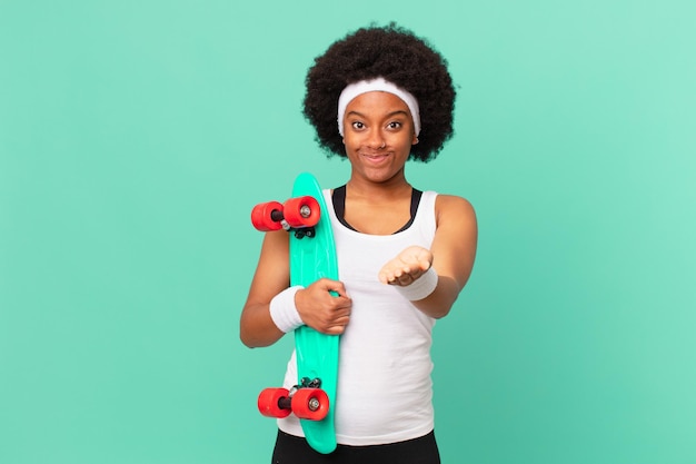 Afro-vrouw die vrolijk lacht met een vriendelijke, zelfverzekerde, positieve blik, een object of concept aanbiedt en toont. skateboard concept