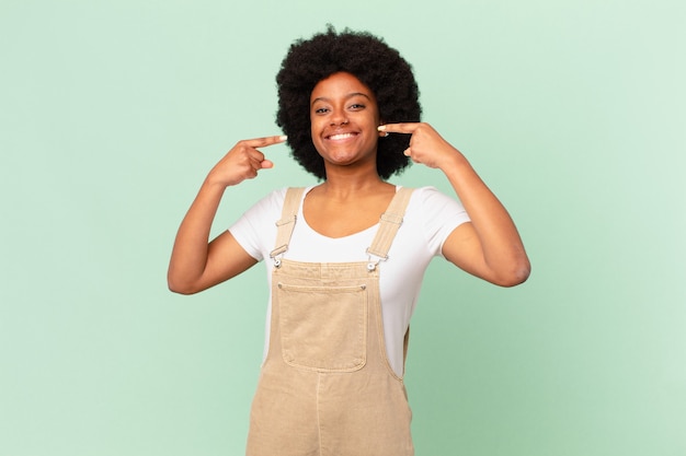 Afro-vrouw die zelfverzekerd glimlacht en wijst naar een brede glimlach, positief, ontspannen, tevreden houding chef-concept