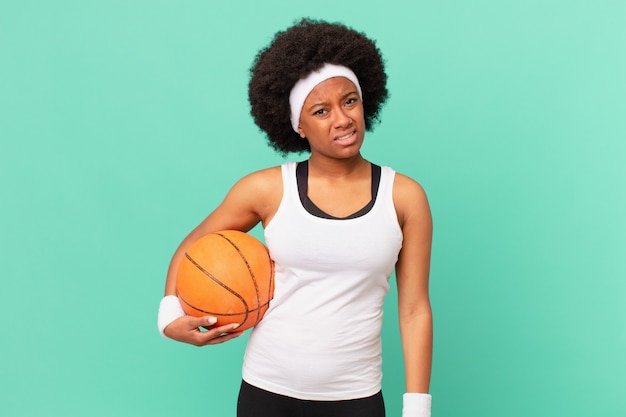 Afro-vrouw die zich verward en verward voelt, met een stomme, verbijsterde uitdrukking die naar iets onverwachts kijkt. basketbal concept