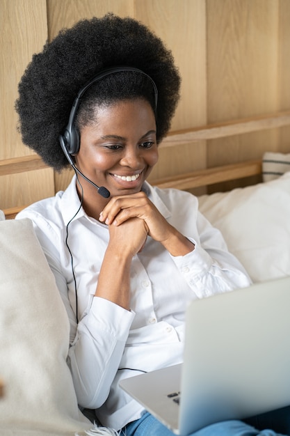 Afro-vrouw draagt een headset, communiceert via videochat op laptop