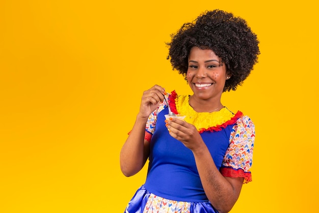 Afro-vrouw gekleed in festa junina-outfit die een heerlijke cural eet