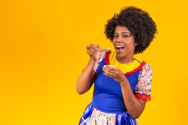 Afro-vrouw gekleed in festa junina-outfit die een heerlijke cural eet