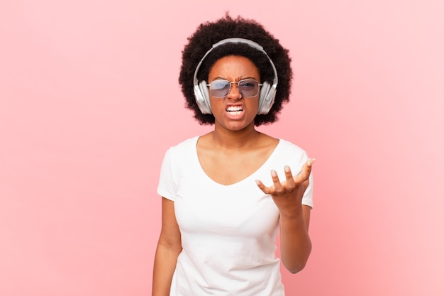 Afro-vrouw kijkt boos, geïrriteerd en gefrustreerd schreeuwend wtf of wat is er mis met je. muziek concept