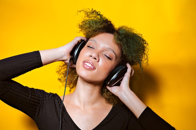 Afro vrouw luisteren muziek met koptelefoon op kleurrijke achtergrond