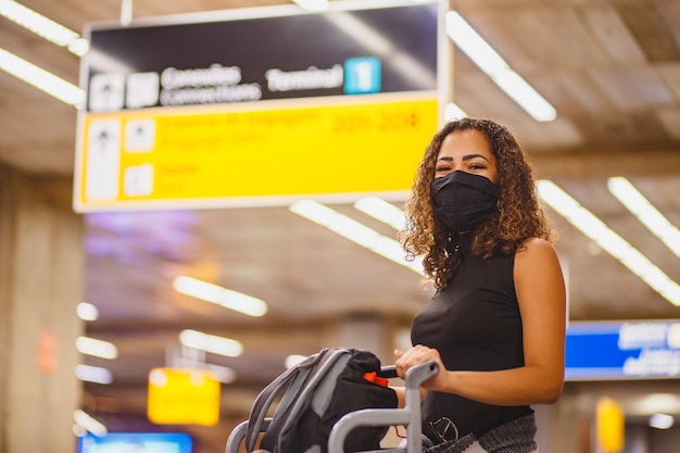 Afro vrouw met koffers op de luchthaven. Vrouw op de luchthaven die in pandemie reist