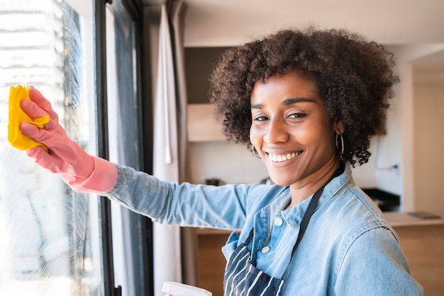 Afro vrouw schoonmaak venster met doek thuis