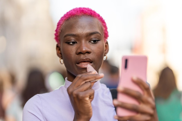 Афро-женщина наносит крем на губы с помощью мобильного телефона