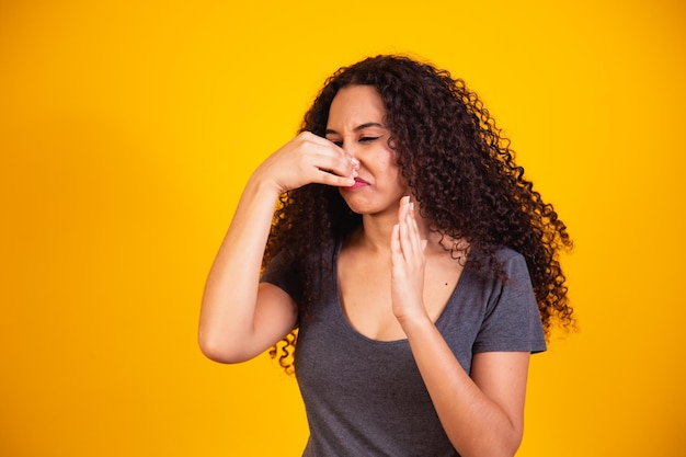 Afro woman feeling disgusted, holding nose to avoid smelling a foul and unpleasant stench