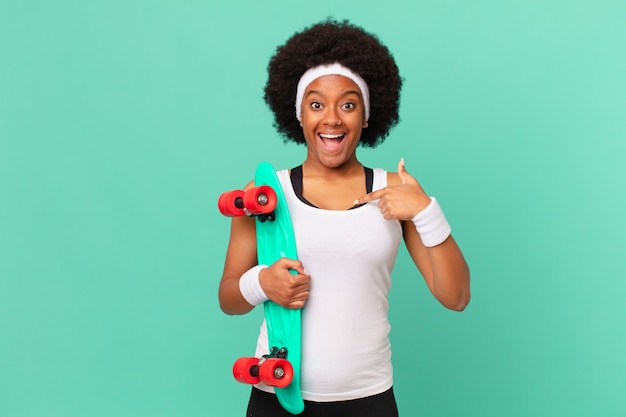 Afro woman feeling happy, surprised and proud, pointing to self with an excited, amazed look. skateboard concept