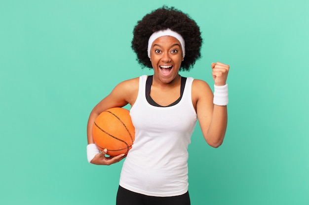 Афро-женщина чувствует себя потрясенной, взволнованной и счастливой, смеется и празднует успех, говоря «Вау!». баскетбольная концепция
