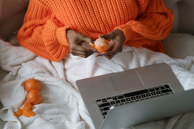 Afro woman hands peeling ripe sweet tangerine, wear orange sweater