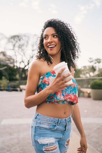 Afro woman listening to music while holding a cup of coffee.