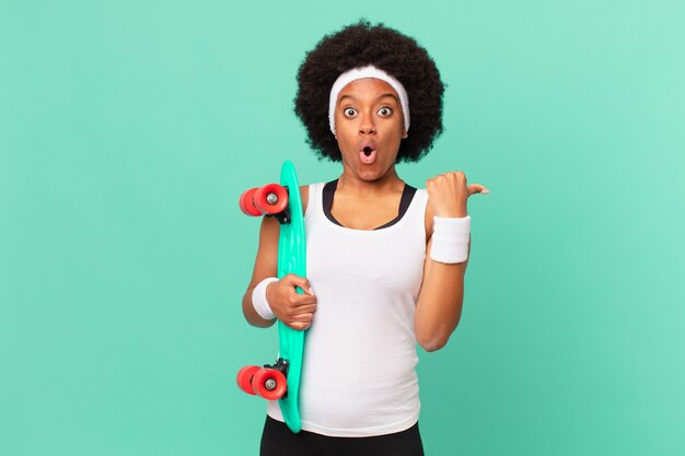 Afro woman looking astonished in disbelief, pointing at object on the side and saying wow, unbelievable. skateboard concept